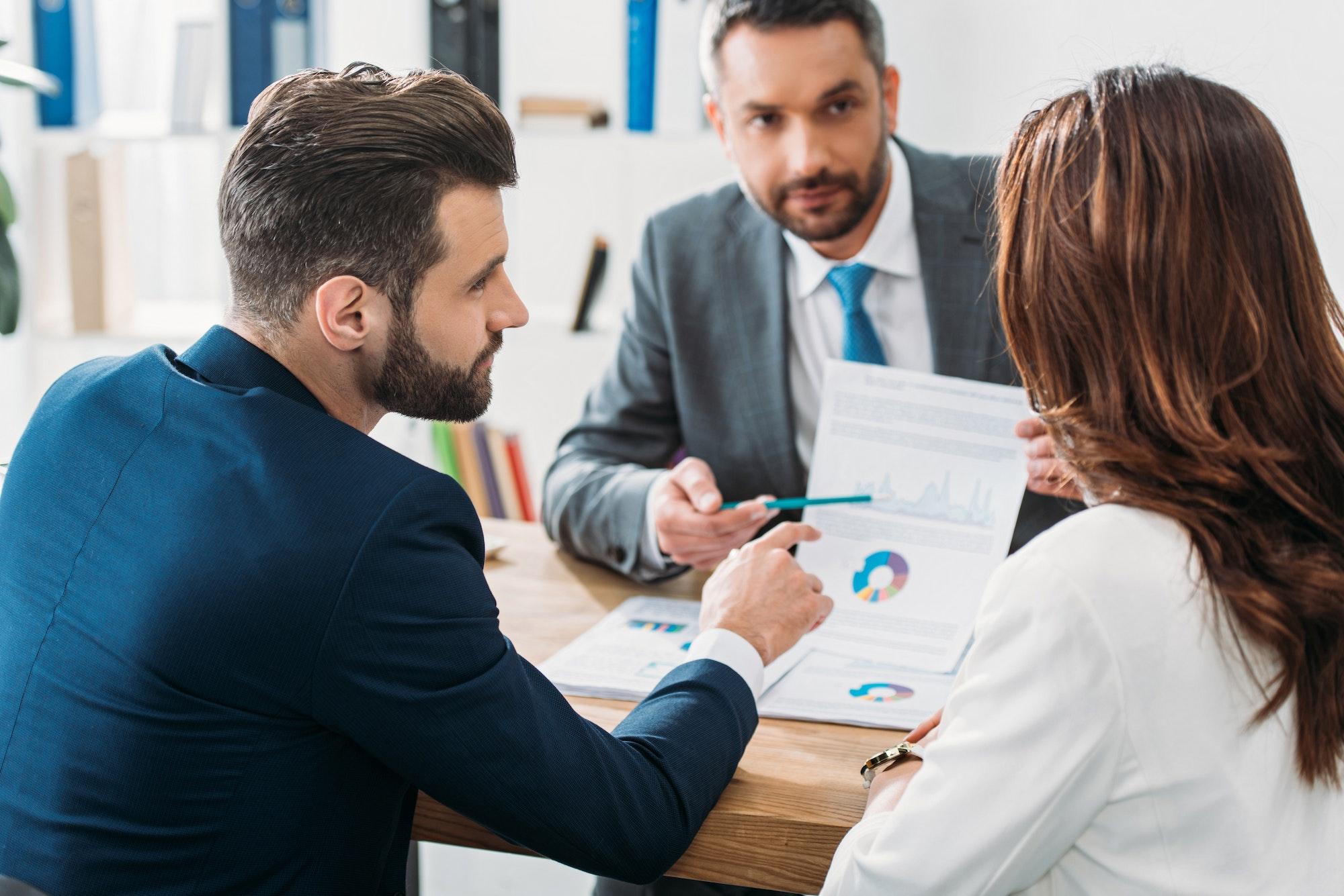 selective focus of investor in suit pointing with finger at document at workspace